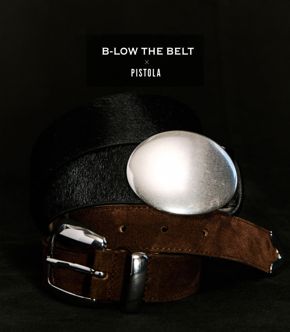 Two belts against a black background with a logo for B-Low the Belt and for Pistola. One belt is black calf-hair with a silver buckle and the other is dark chocolate suede with a silver buckle.