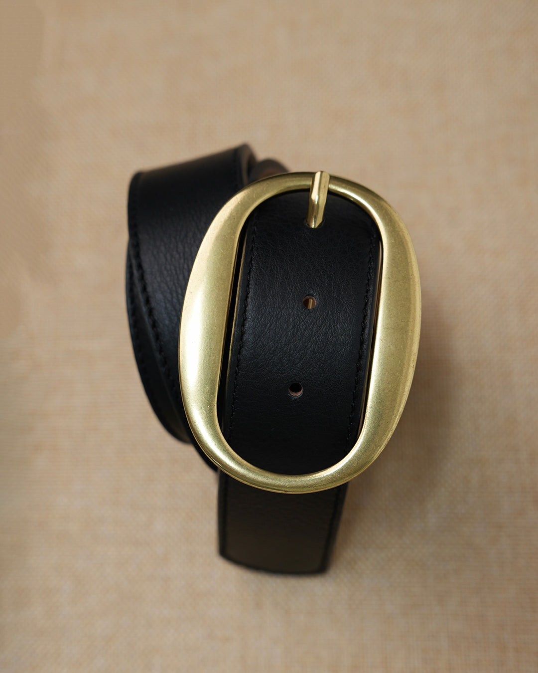 Black leather belt with a gold buckle on a beige background