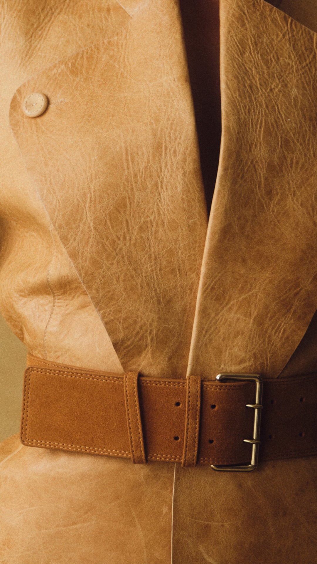 A close-up of a tan leather jacket with a matching wide brown leather belt featuring a silver buckle.
