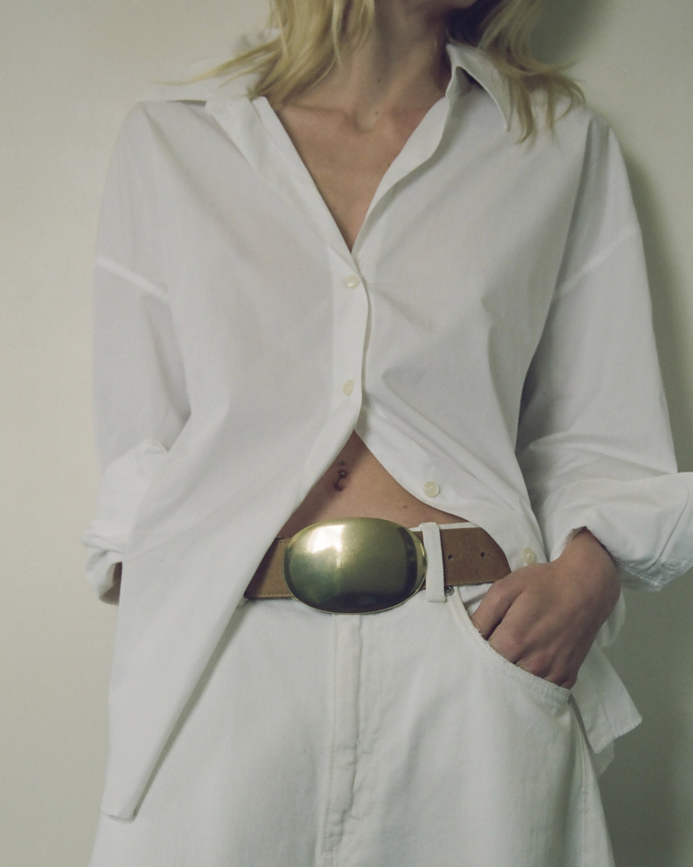 Person wearing a white shirt with an open front and a gold belt, standing against a plain background.
