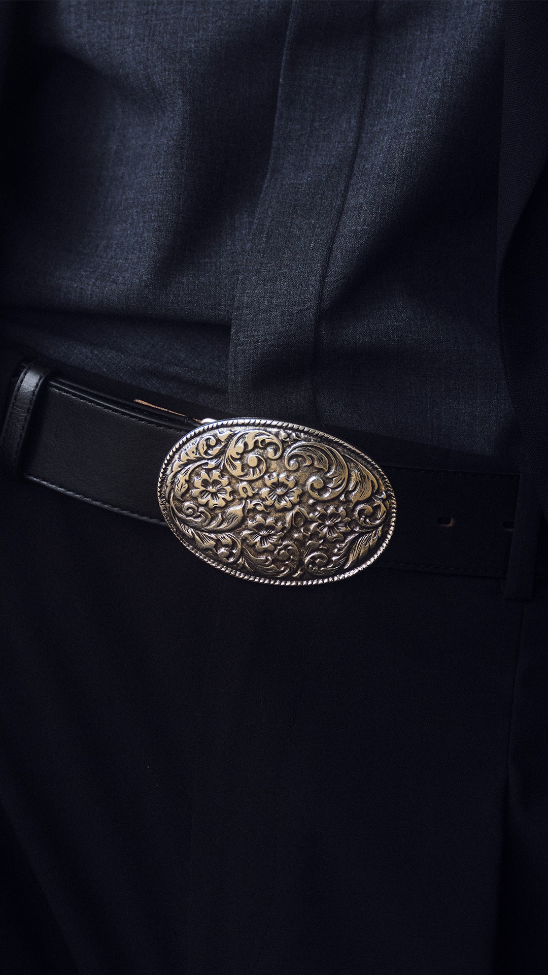 a silver western plaque buckle belt with a black strap on a dark suit