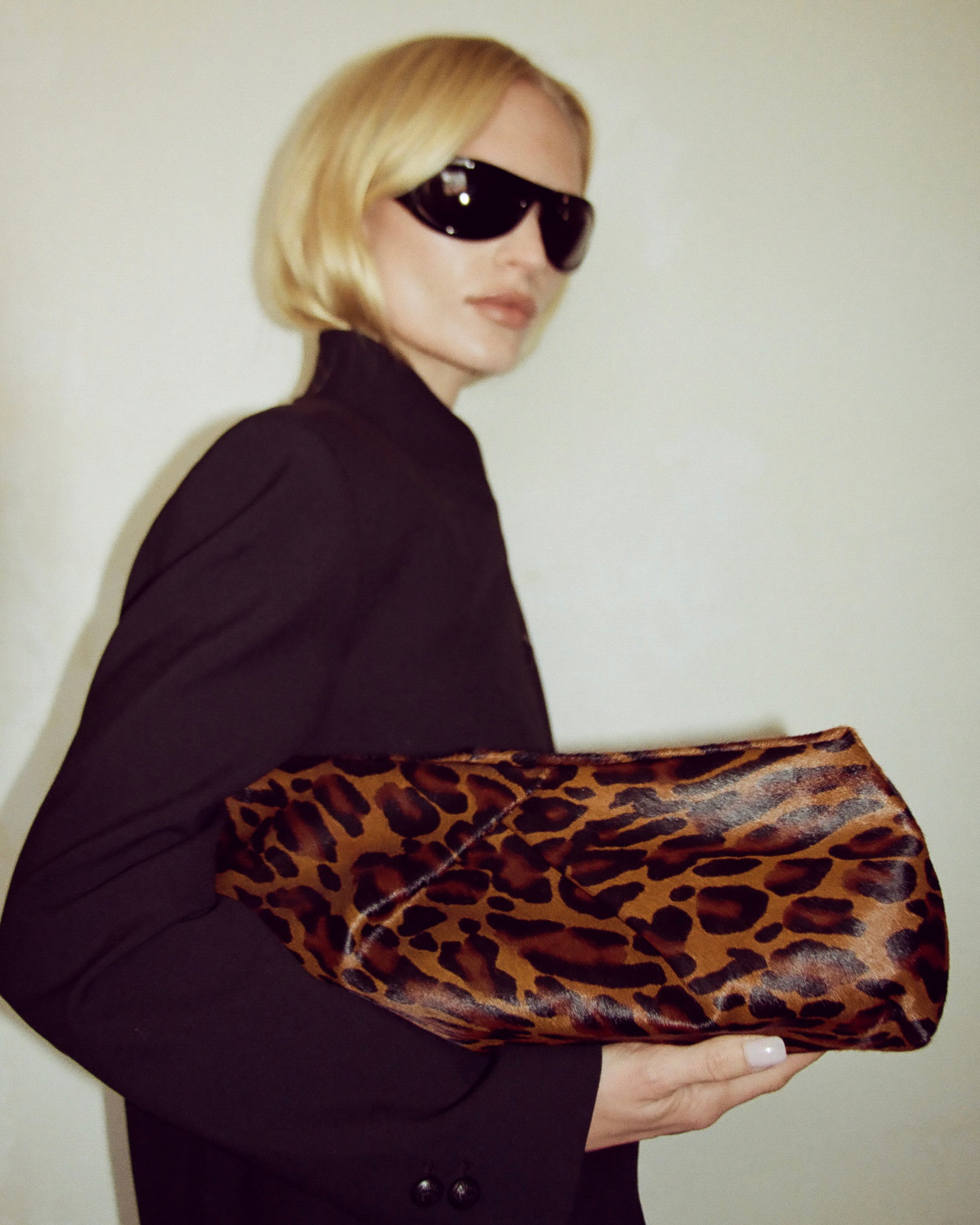 Person holding a leopard print clutch against a plain background