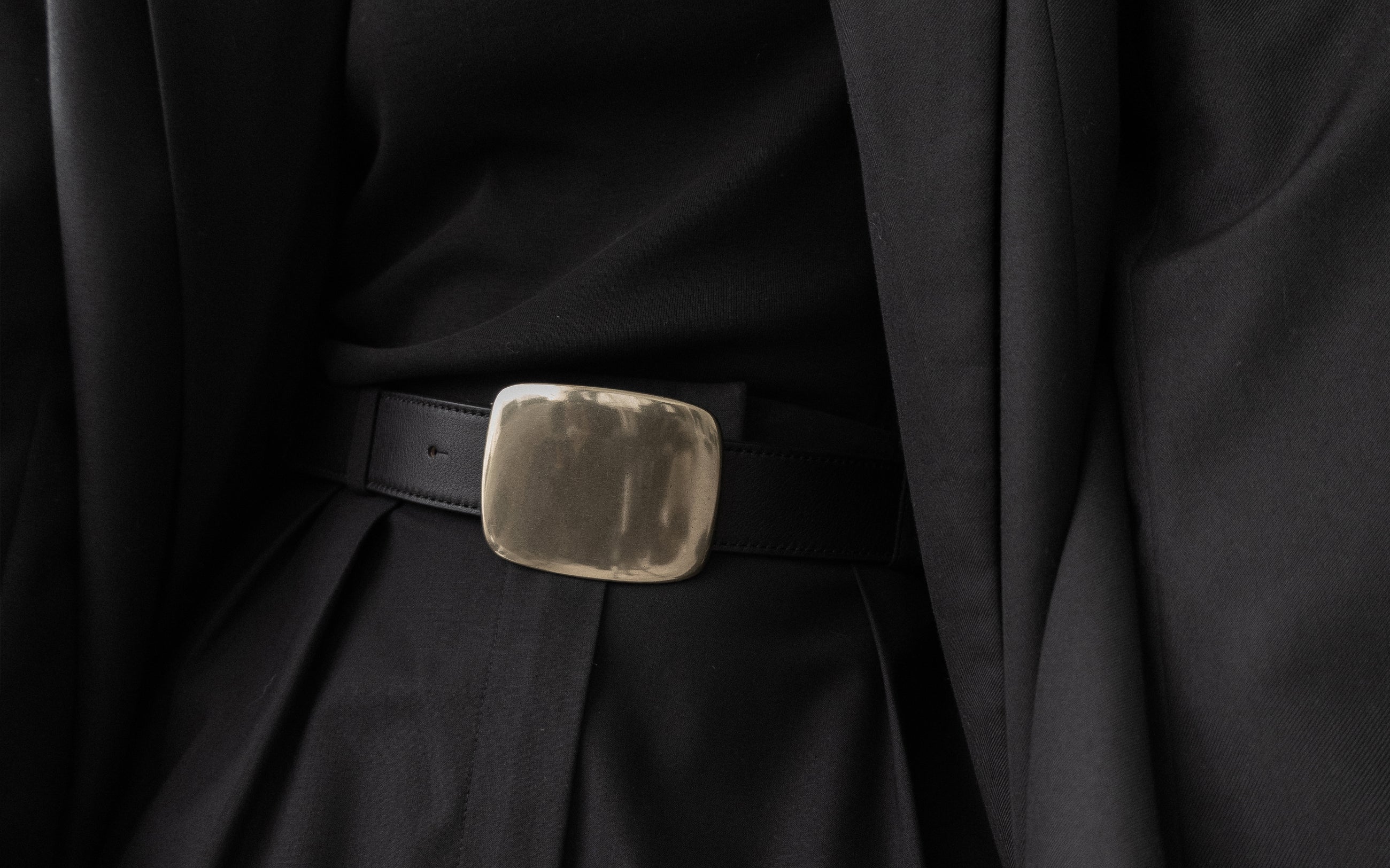 Close-up of a black coat with a belt and buckle on a dark background
