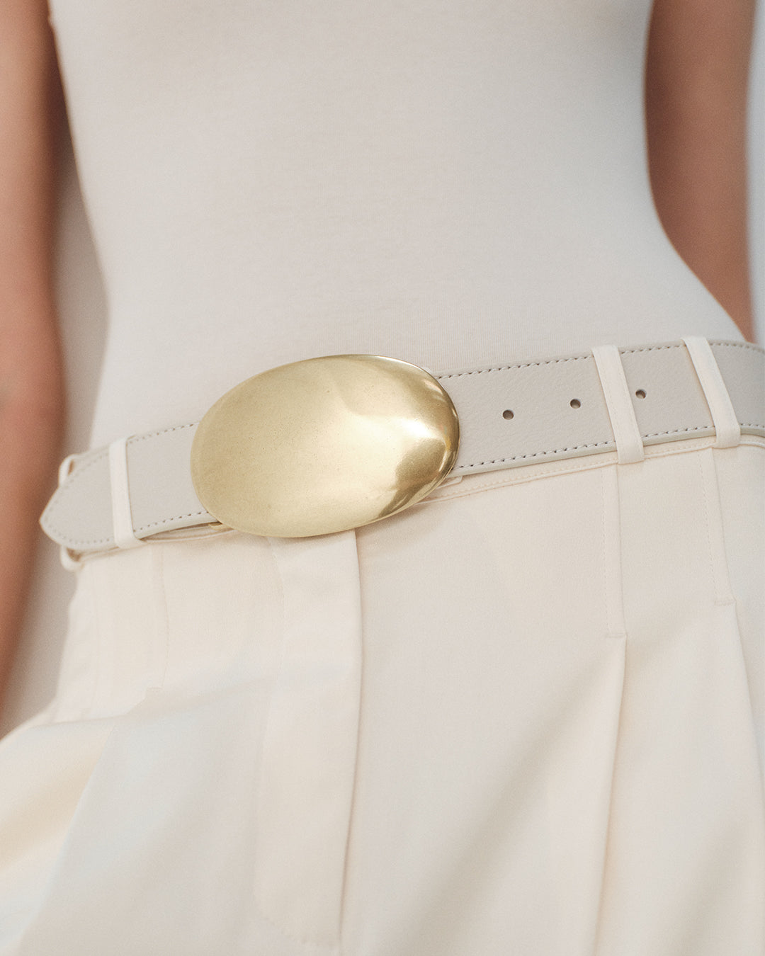 White belt with a gold buckle worn by a person against a neutral background